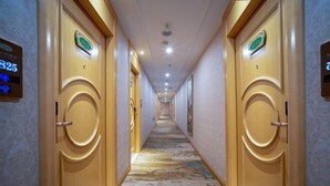 Ein Hotelgang mit Türen, die mit 25 und 26 gekennzeichnet sind, einem gemusterten Teppich und einer Decke mit eingelassenen Leuchten.