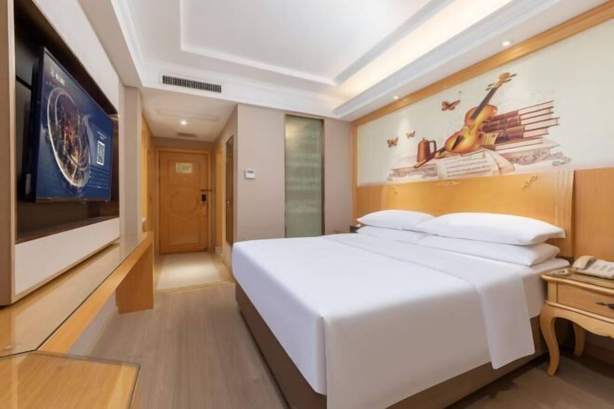A hotel room with a large bed, a television, a wooden nightstand, and a mural on the wall.