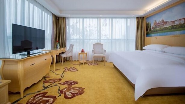 Ein Hotelzimmer mit einem großen Bett, einem Fernseher, einem Schreibtisch mit Stuhl und einem kleinen Tisch.