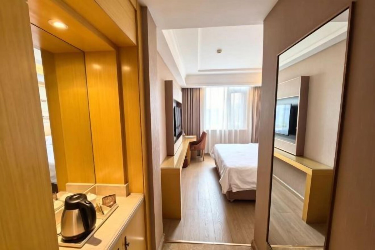 Quarto de hotel com cama, escrivaninha, televisão e espelho.