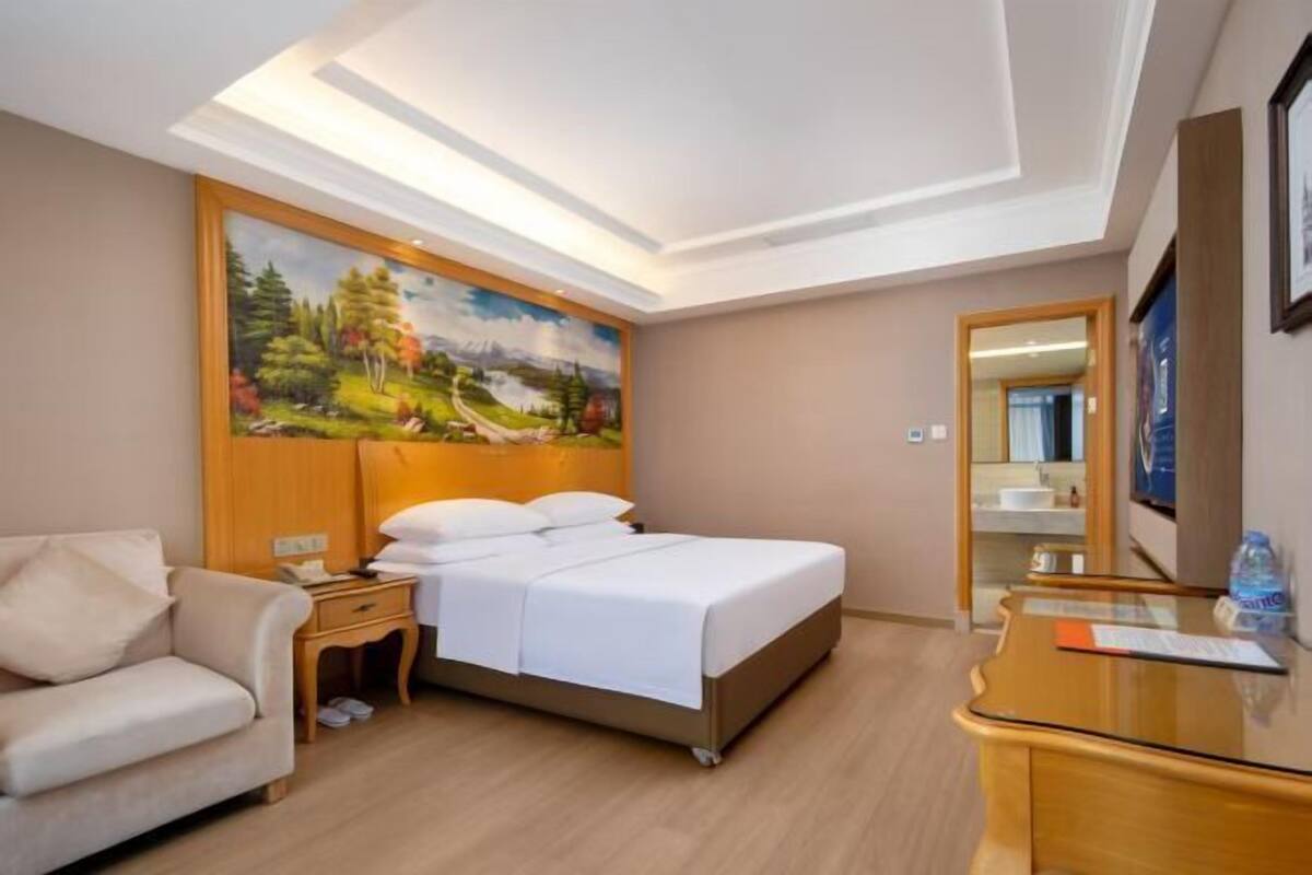 A hotel room with a bed, a sofa, a desk, and a painting on the wall.