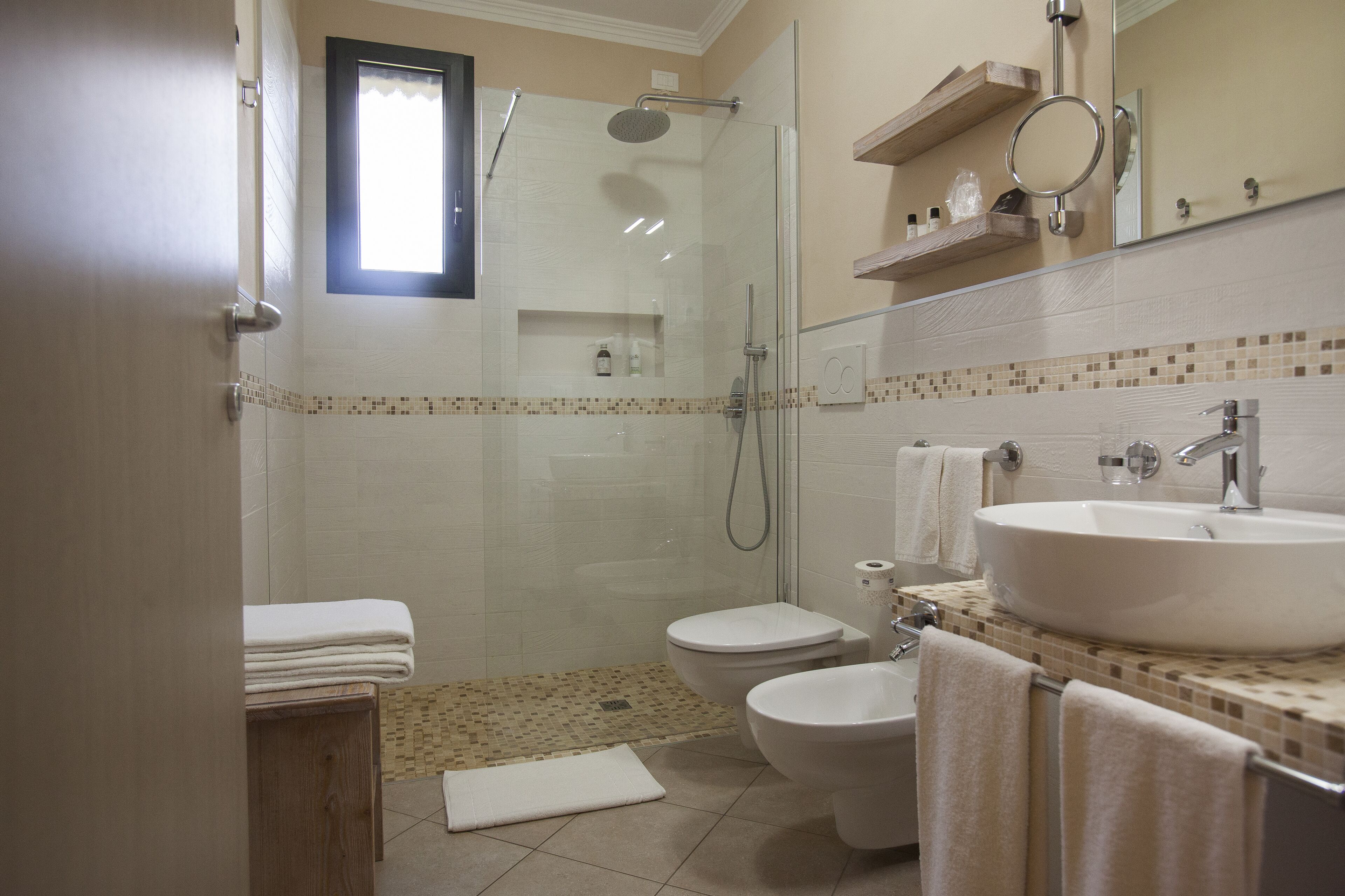 Badeværelse med brusekabine i glas, toilet, håndvask med spejl og et håndklædestativ.