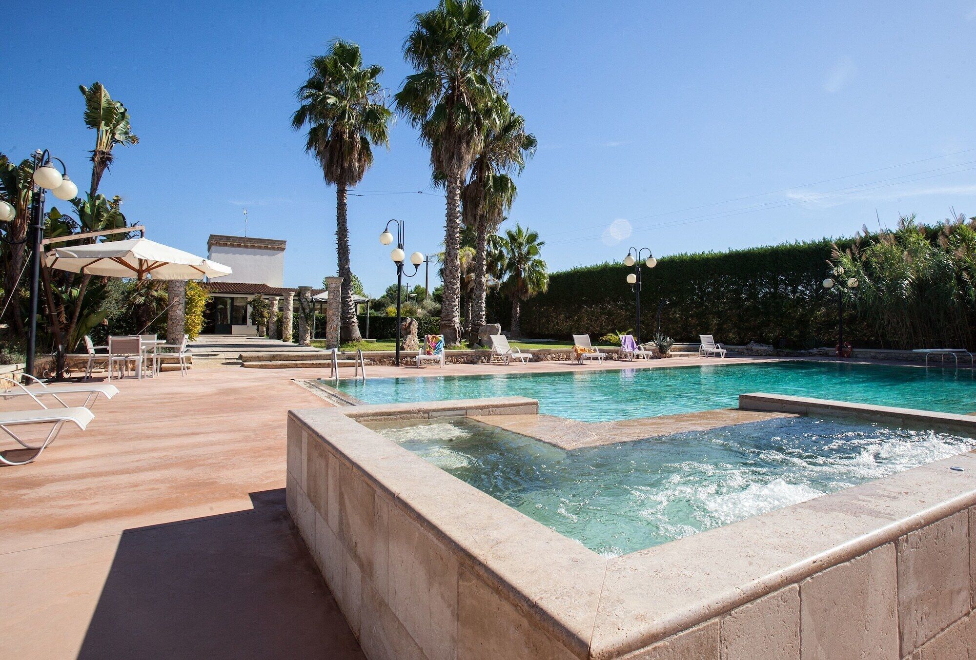 A pool area with lounge chairs, palm trees, and outdoor lighting.