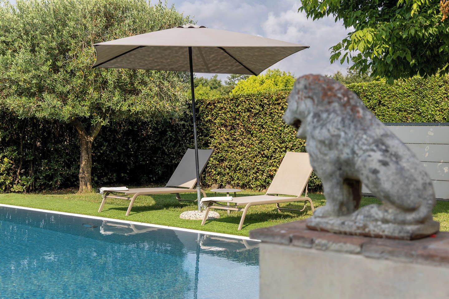 Un área de piscina con dos sillas de descanso y una estatua de piedra.