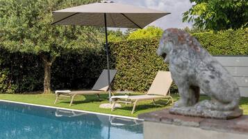 Un área de piscina con dos sillas de descanso y una estatua de piedra.