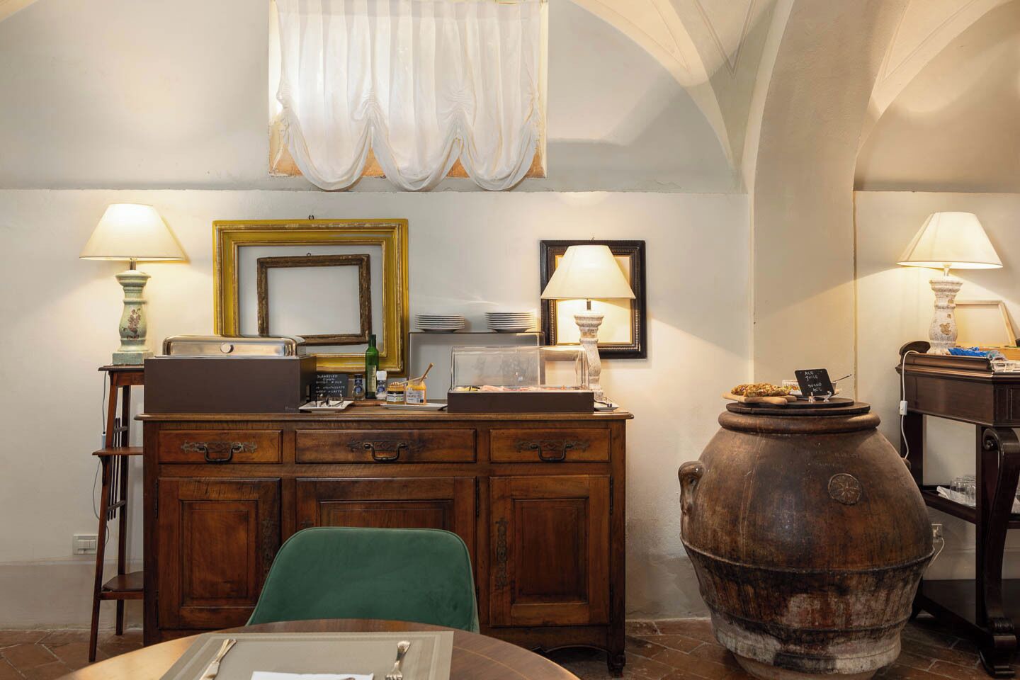 A dining area with a wooden table, chairs, a vintage-style lamp, a large metal pot, and a mirror on the wall.