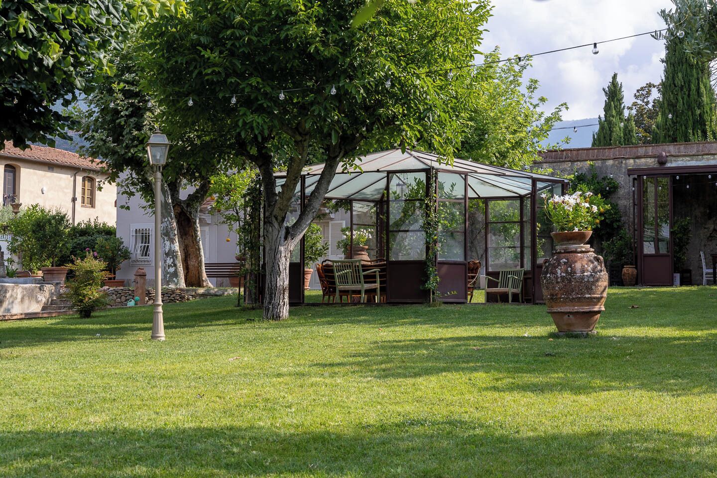 A greenhouse with a glass roof, surrounded by trees and a lawn.