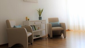 A living room with two armchairs, a small white side table with a plant, and a bookshelf. - Arcangel Hotel (Lagoa)