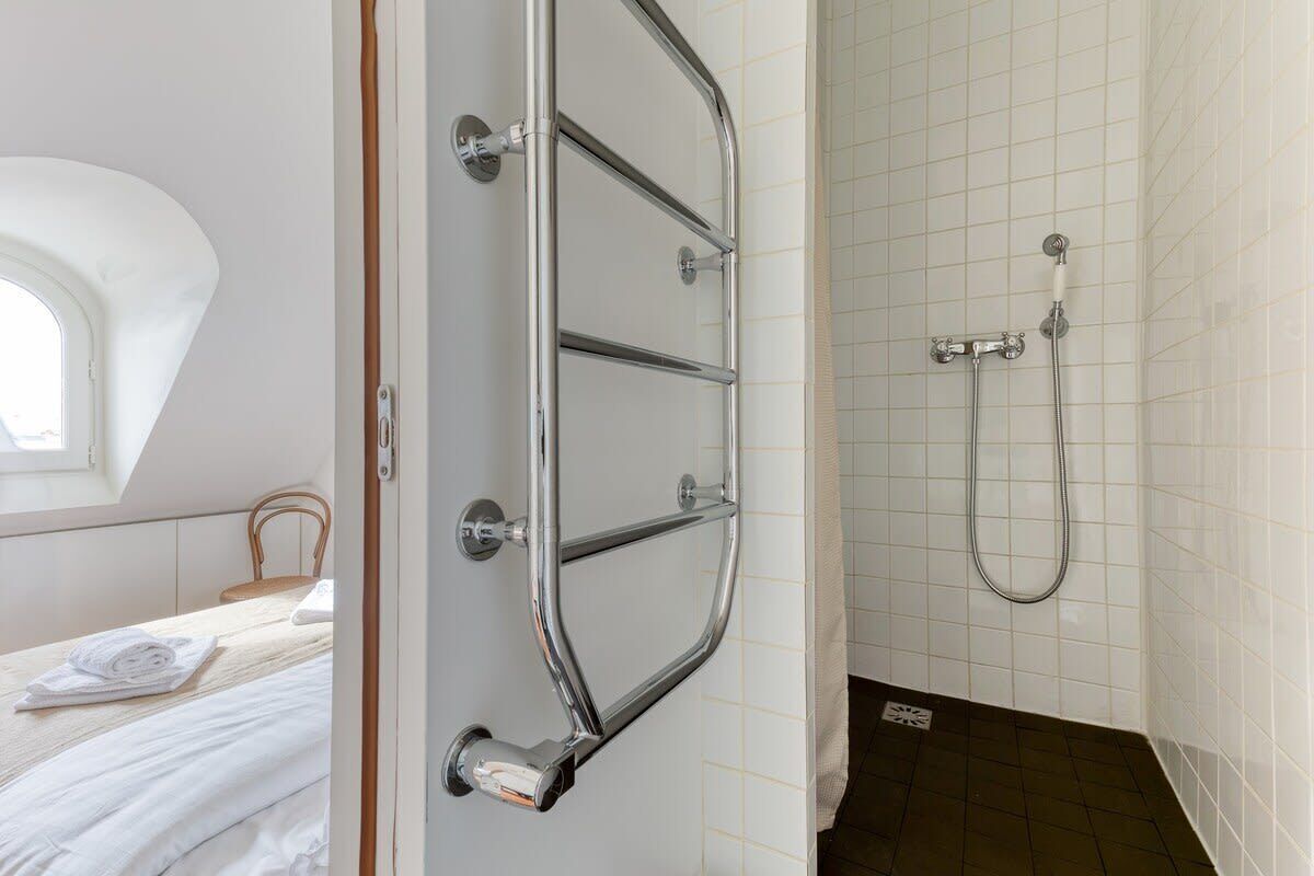 A bathroom with a shower, a towel rack, and a bed with towels.