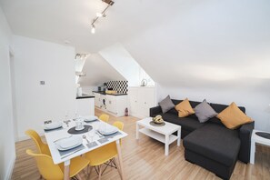 A modern apartment with a dining area, a black sofa with cushions, and a kitchen in the background. - Flat 5 - 61 Old Dover Road (Canterbury)