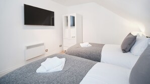 A modern bedroom with two beds, a flat-screen TV, a wardrobe, and a radiator.