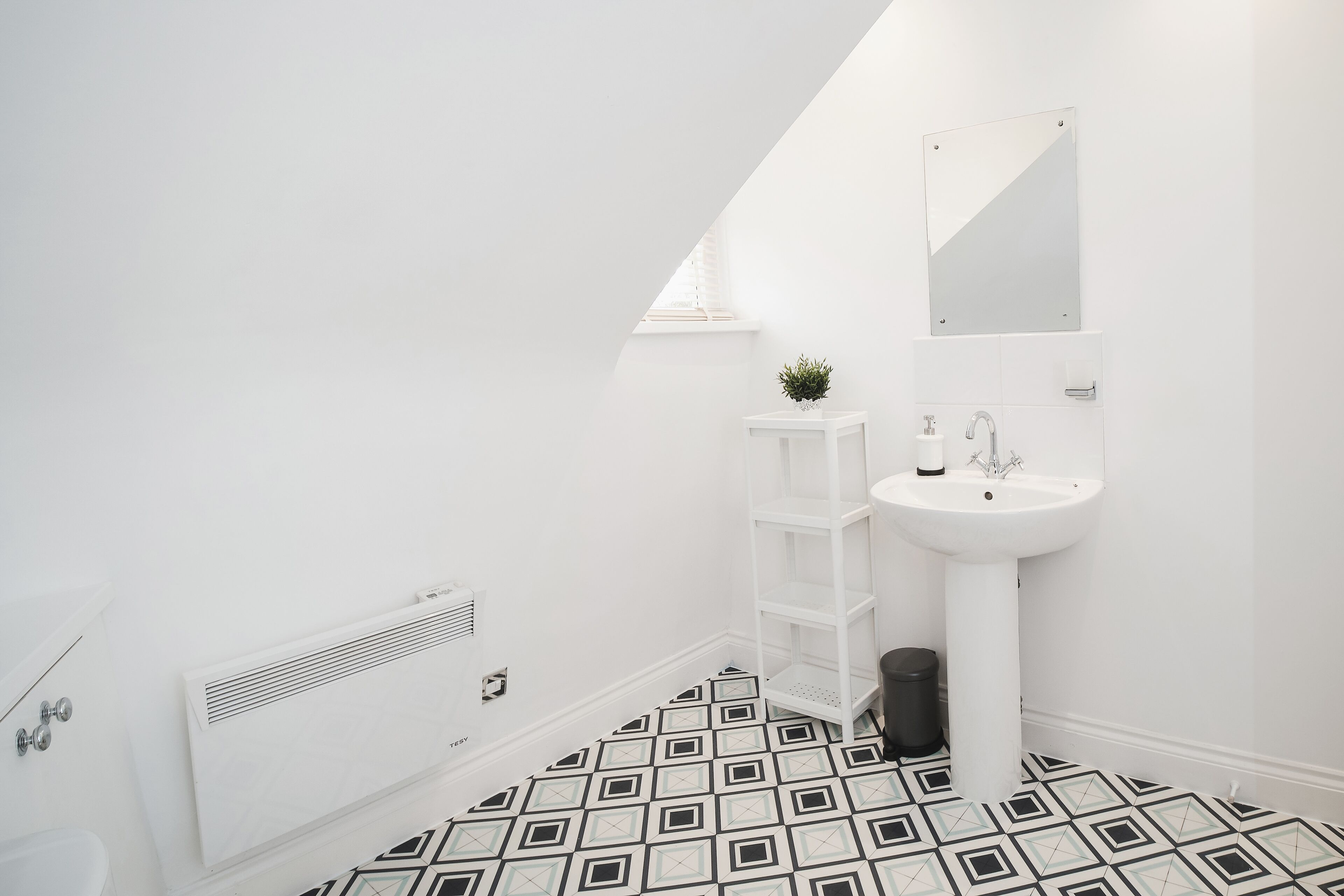 A modern bathroom with a white sink, mirror, and radiator.