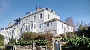 A large, multi-story building with a symmetrical facade, multiple windows, and a stone wall with an arched entrance.