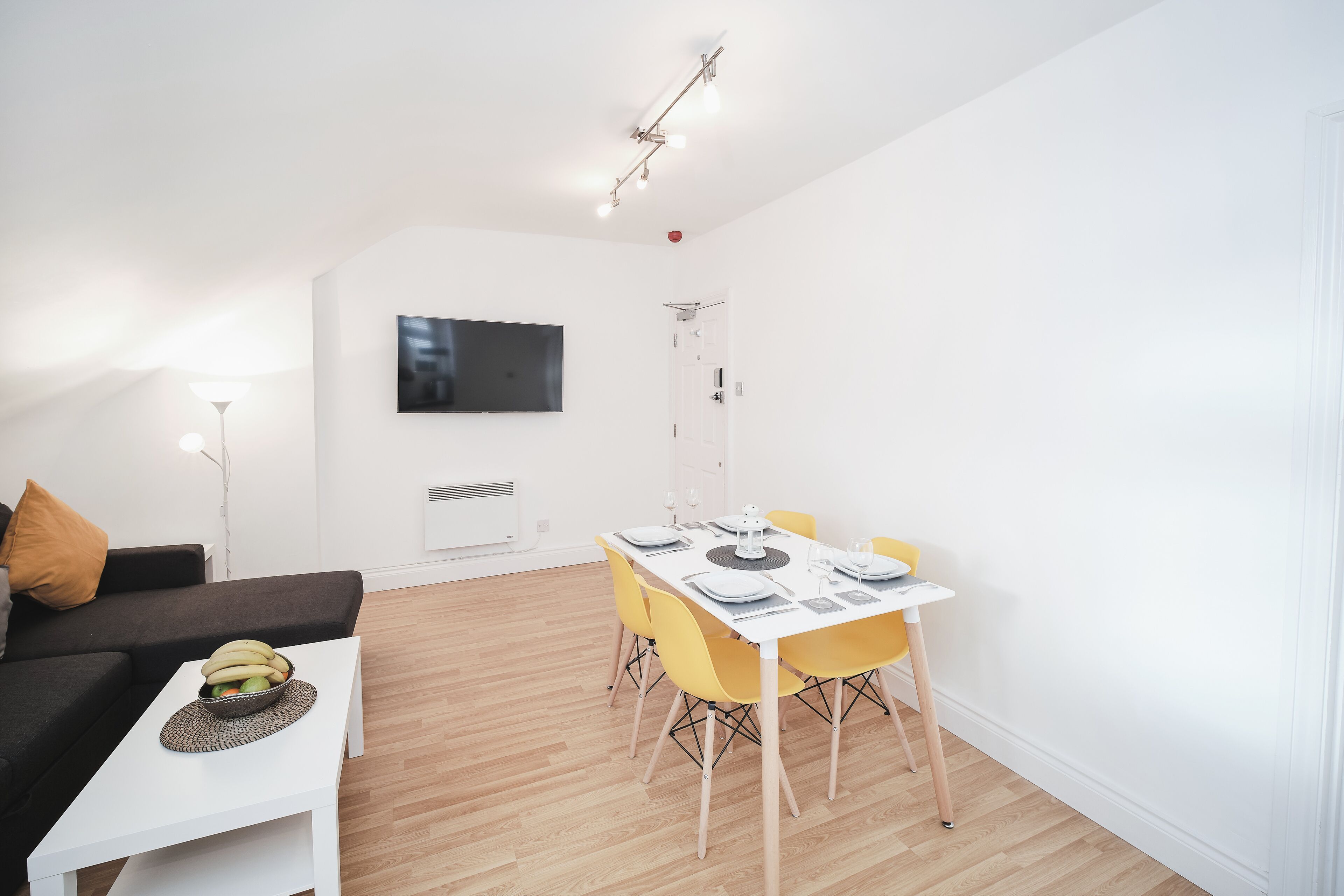 Ein modernes Wohnzimmer mit Essbereich, weißen Wänden und einem an der Wand befestigten Flachbildfernseher.