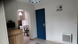 En kompakt opholdsstue med tekøkken, spiseplads og en blå dør.