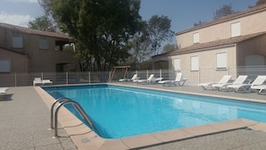 En swimmingpool med liggestole, en metalstige og en fliseterrasse.