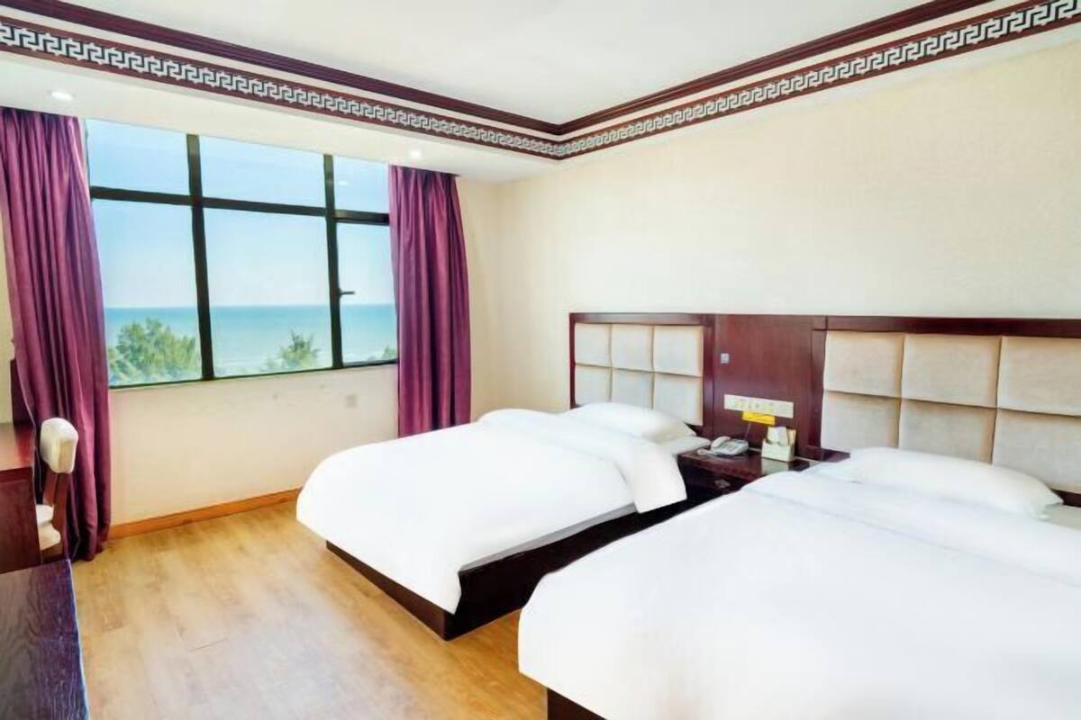 Une chambre d’hôtel avec deux lits, une grande fenêtre donnant sur un beau paysage et une tête de lit en bois.
