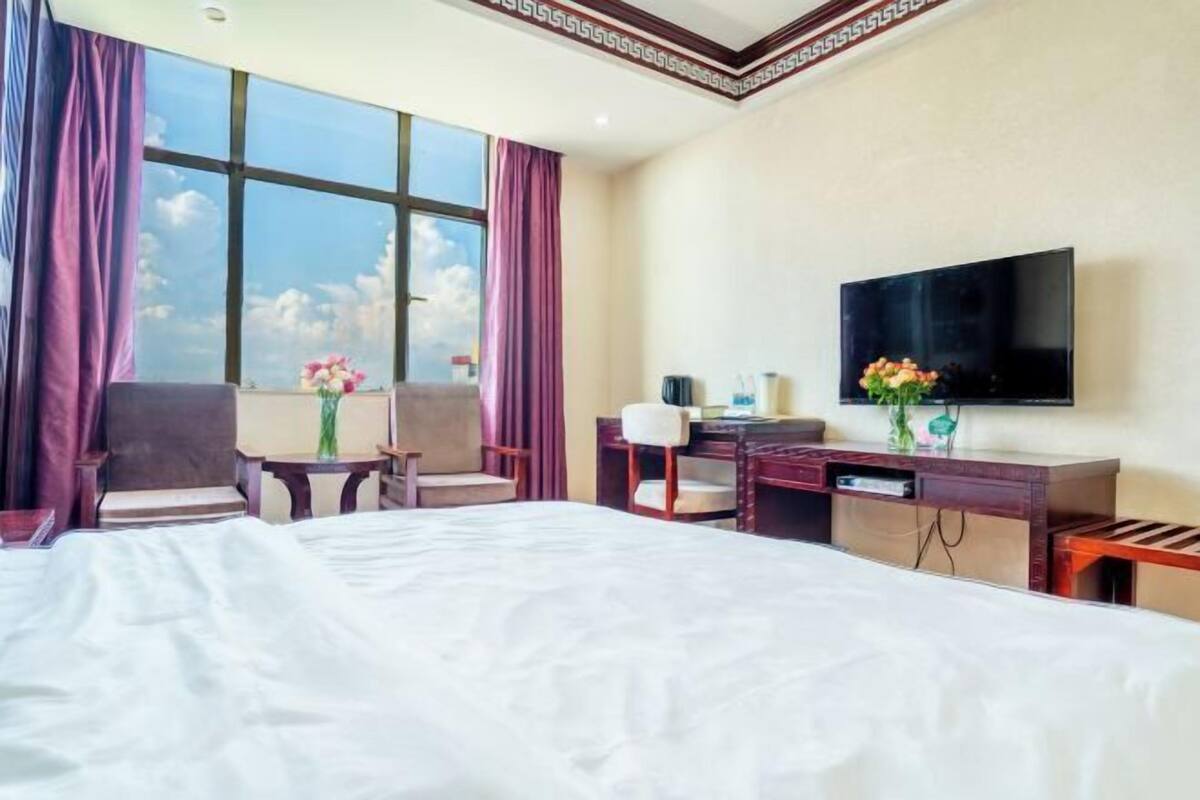 Une chambre d’hôtel avec un grand lit, un bureau, une chaise, une télévision et une fenêtre avec des rideaux.