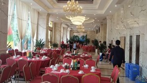 Une salle de banquet spacieuse, avec des tables rondes, des chaises rouges et des lustres.