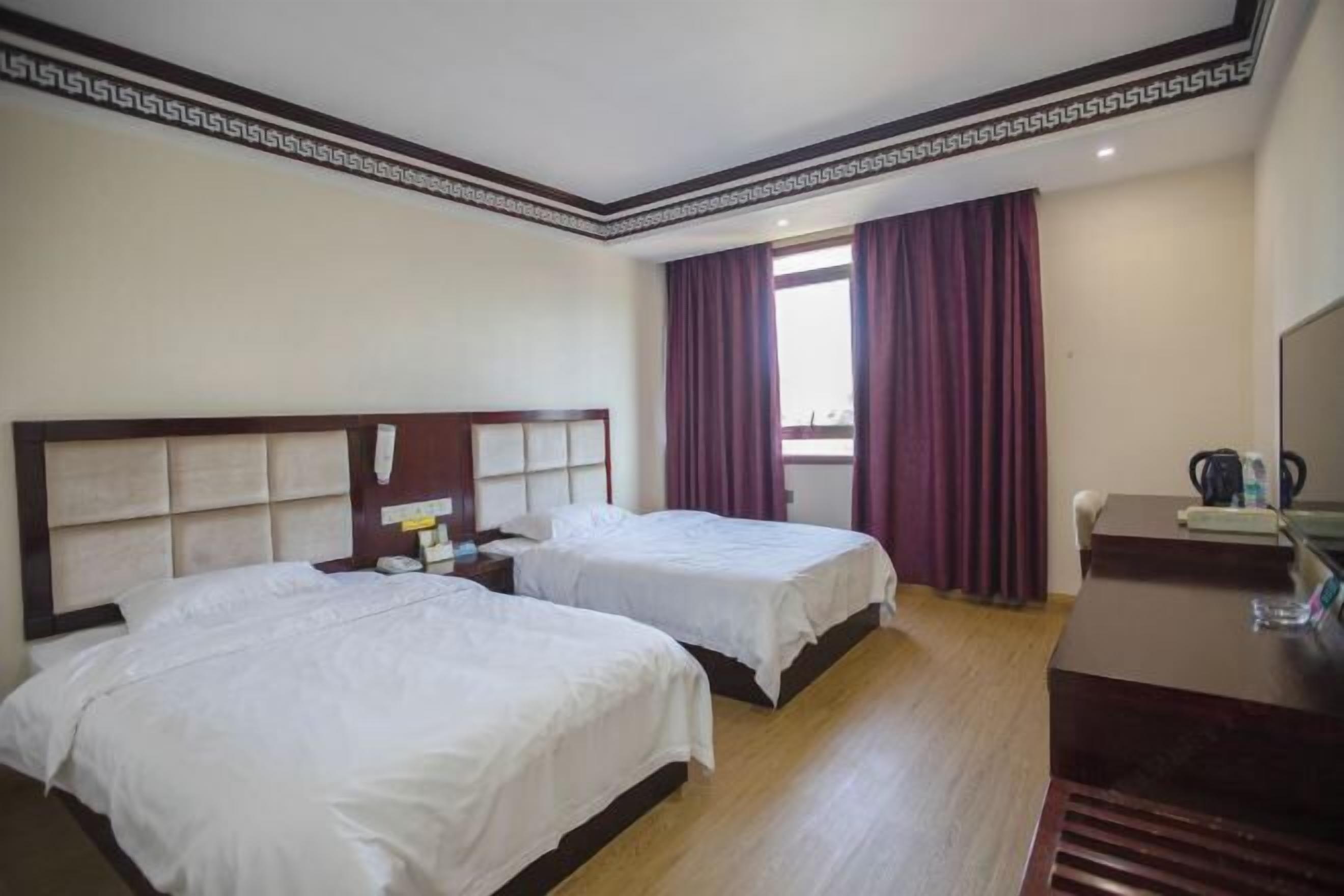 Habitación de hotel con dos camas, un escritorio y una ventana con cortinas.