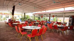 Un espace extérieur abrité, aménagé pour les repas, avec des chaises rouges et des tables rondes, doté d’un sol carrelé et d’une structure de toit en métal.