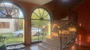 A staircase with ornate metal railings, a view of a car outside through a large arched window, and a green rug on the floor. - Remarkable 6 Bedrooms Villapiemonte With Land (Cerrione)