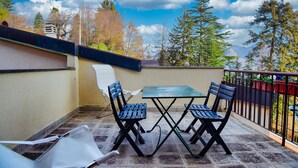 A balcony with a table and chairs, a white chair, and a view of trees and mountains. - Casa Claudia by Wonderful Italy (Bellagio)