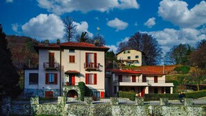 A two-story building with a stone facade, red shutters, and a balcony. - Casa Claudia by Wonderful Italy (Bellagio)