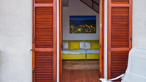 A room with a wooden door, a yellow sofa, and a painting of flowers on the wall. - Casa Claudia by Wonderful Italy (Bellagio)