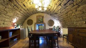 A stone-walled room with a wooden dining table and chairs, a chandelier, and a fireplace. - The Manor at Plane Castle - Sleeps 8 - Pets Ok (Falkirk)