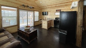 A cabin with a wooden interior, a ceiling fan, a kitchen area, and a seating area with a table and sofa. - Cozy lake front Cabin that's perfect for two! (Grove)