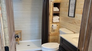 A wooden bathroom with a toilet, sink, and shower. - Cozy lake front Cabin that's perfect for two! (Grove)