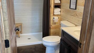 A wooden bathroom with a toilet, sink, and shower.
