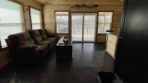 A cozy cabin interior with a wooden ceiling, a sofa, a coffee table, and a refrigerator. - Cozy lake front Cabin that's perfect for two! (Grove)