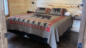 A wooden cabin room with a bed, a ceiling fan, a mounted picture, and a small table with a lamp. - Cozy lake front Cabin that's perfect for two! (Grove)