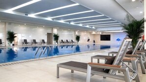 A modern indoor swimming pool with lounge chairs and potted plants. - Shenglin International Hotel (Gaobeidian)