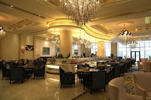 A spacious hotel lobby with multiple seating areas, a central bar, and large chandeliers.
