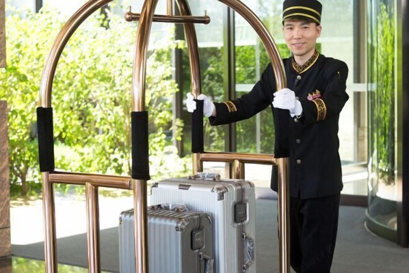 A person in a uniform standing next to a large, metallic gate with a suitcase.