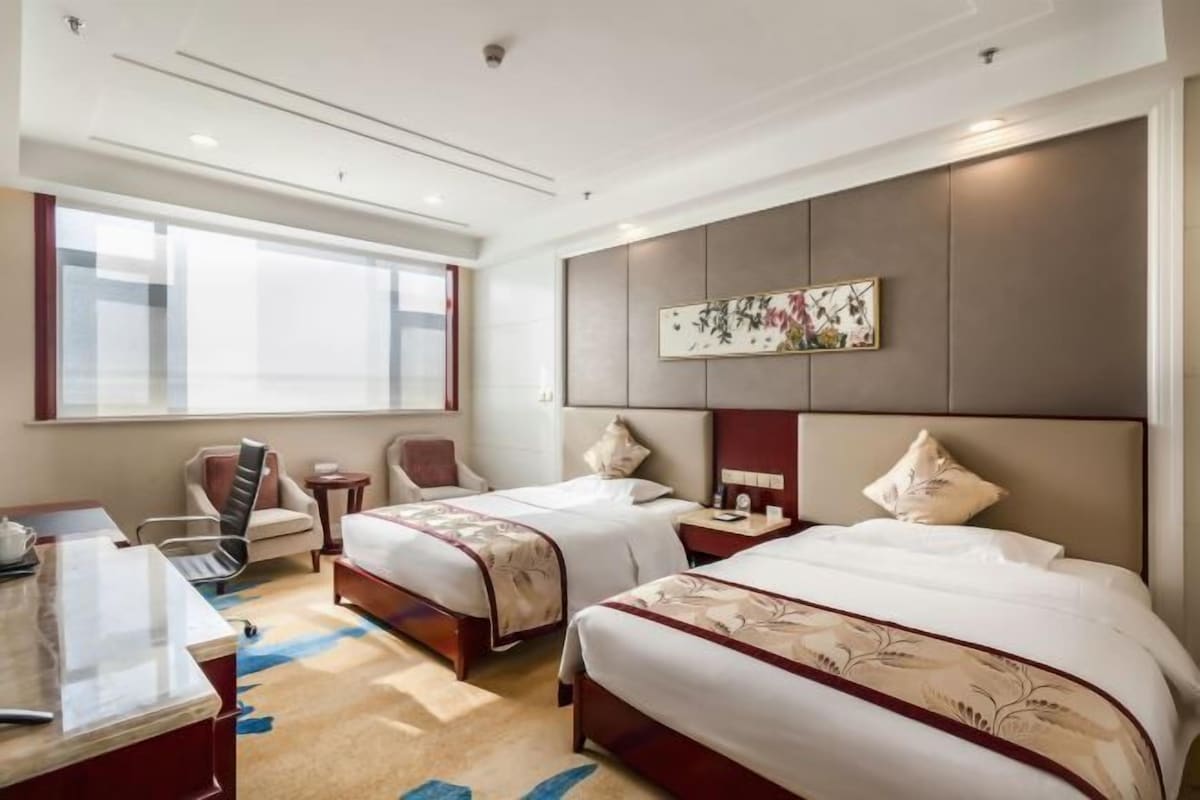 A hotel room with two beds, a desk, a chair, and a large window.