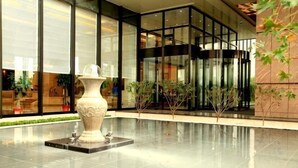 A modern lobby with a large vase sculpture, glass walls, and indoor plants. - Shenglin International Hotel (Gaobeidian)