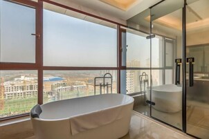 A modern bathroom with a bathtub, large windows, and a view of buildings.