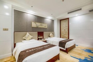 Quarto de hotel com duas camas, cabeceira de madeira, um quadro na parede e um tapete com padrão azul.