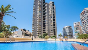 A swimming pool with a white fence and palm trees, surrounded by high-rise buildings. - Don Miguel Apartment 8-C Levante Beach (Benidorm)