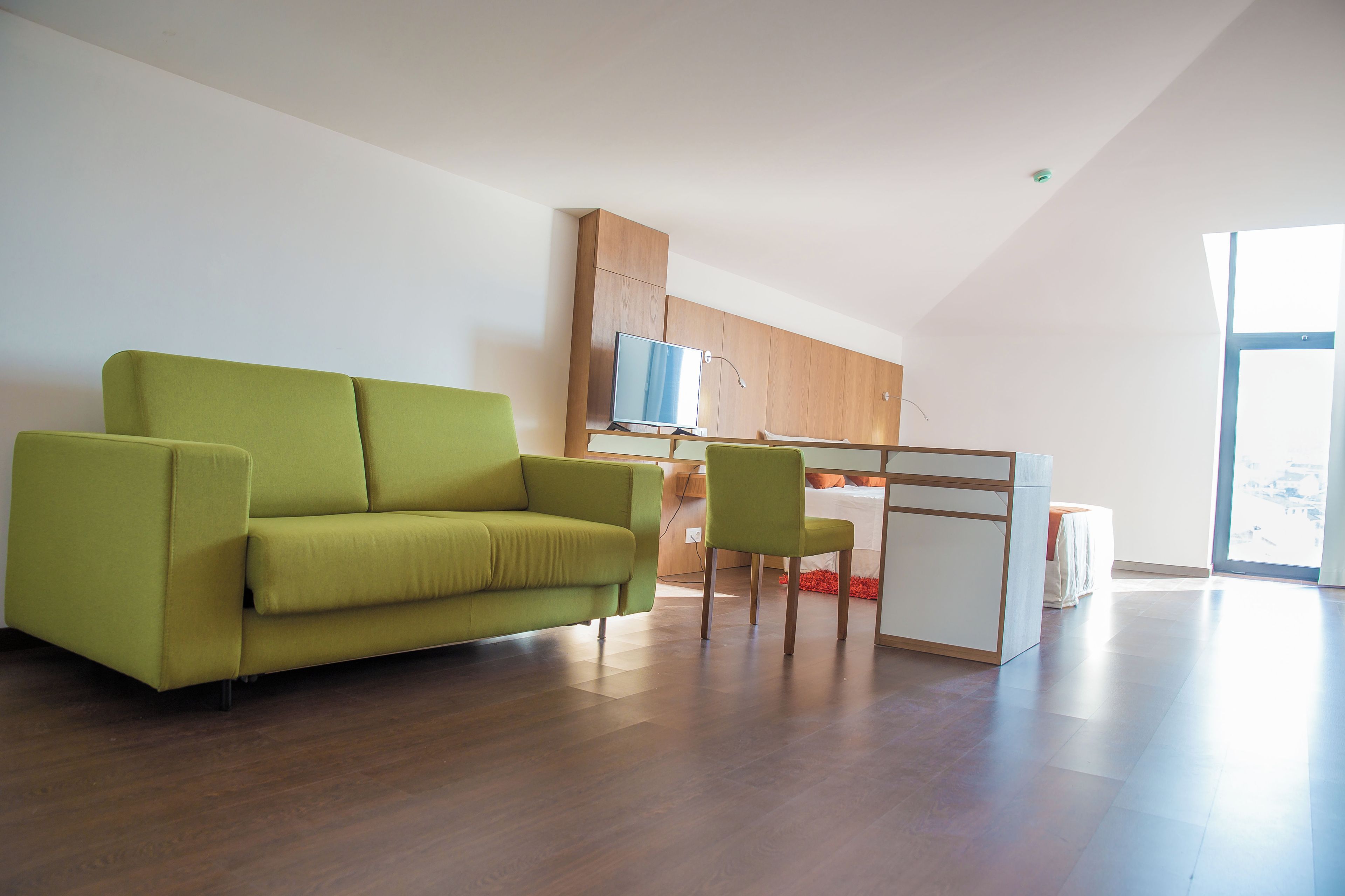 A modern living space with a green sofa, a wooden dining table, and a chair.