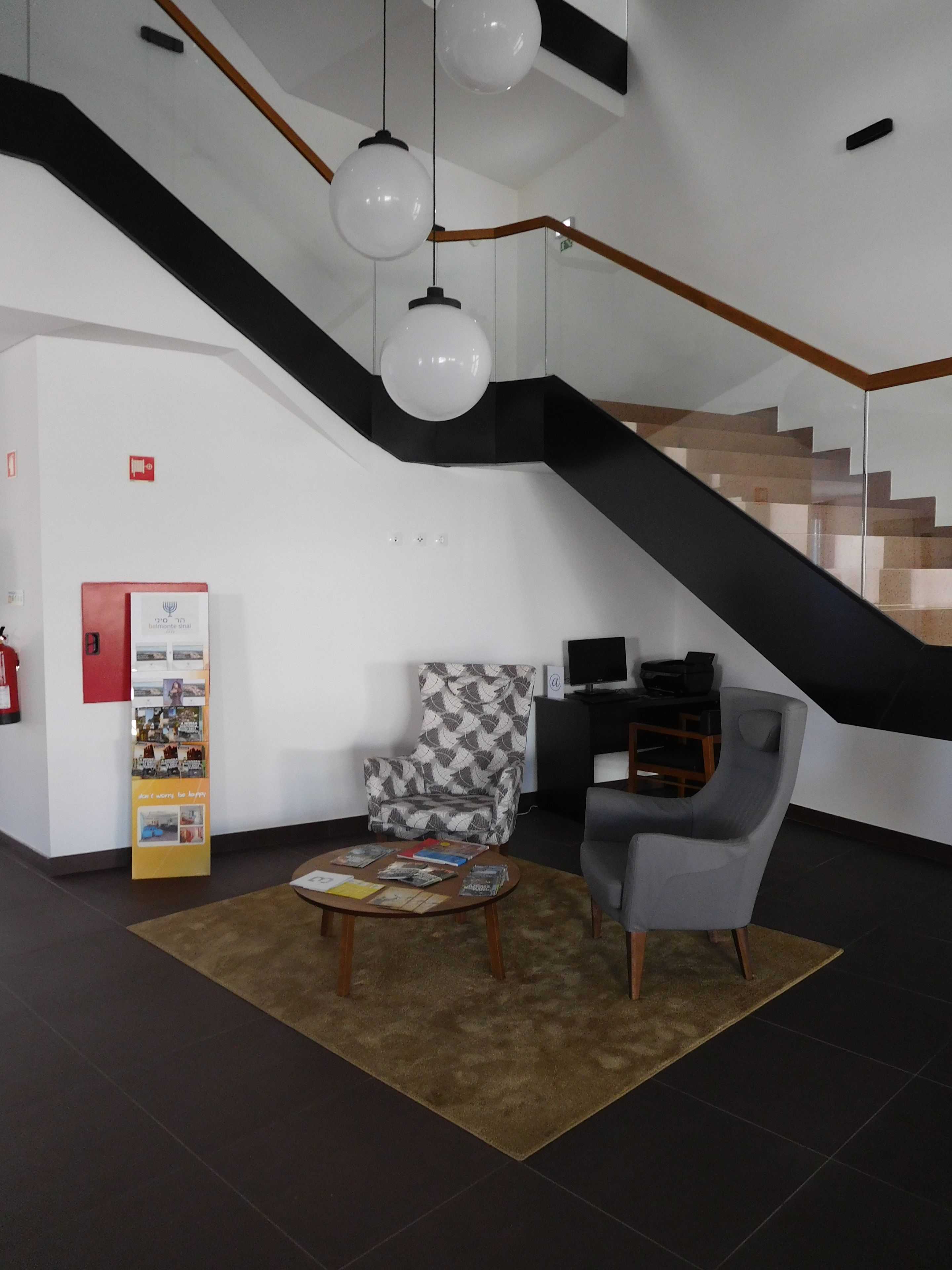 A modern interior with a staircase, a patterned armchair, a coffee table with books, and a red information stand.