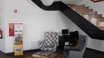 A modern interior with a staircase, a patterned armchair, a coffee table with books, and a red information stand.