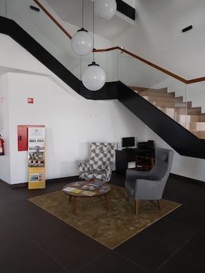 A modern interior with a staircase, a patterned armchair, a coffee table with books, and a red information stand. - Belmonte Sinai Hotel (Belmonte)