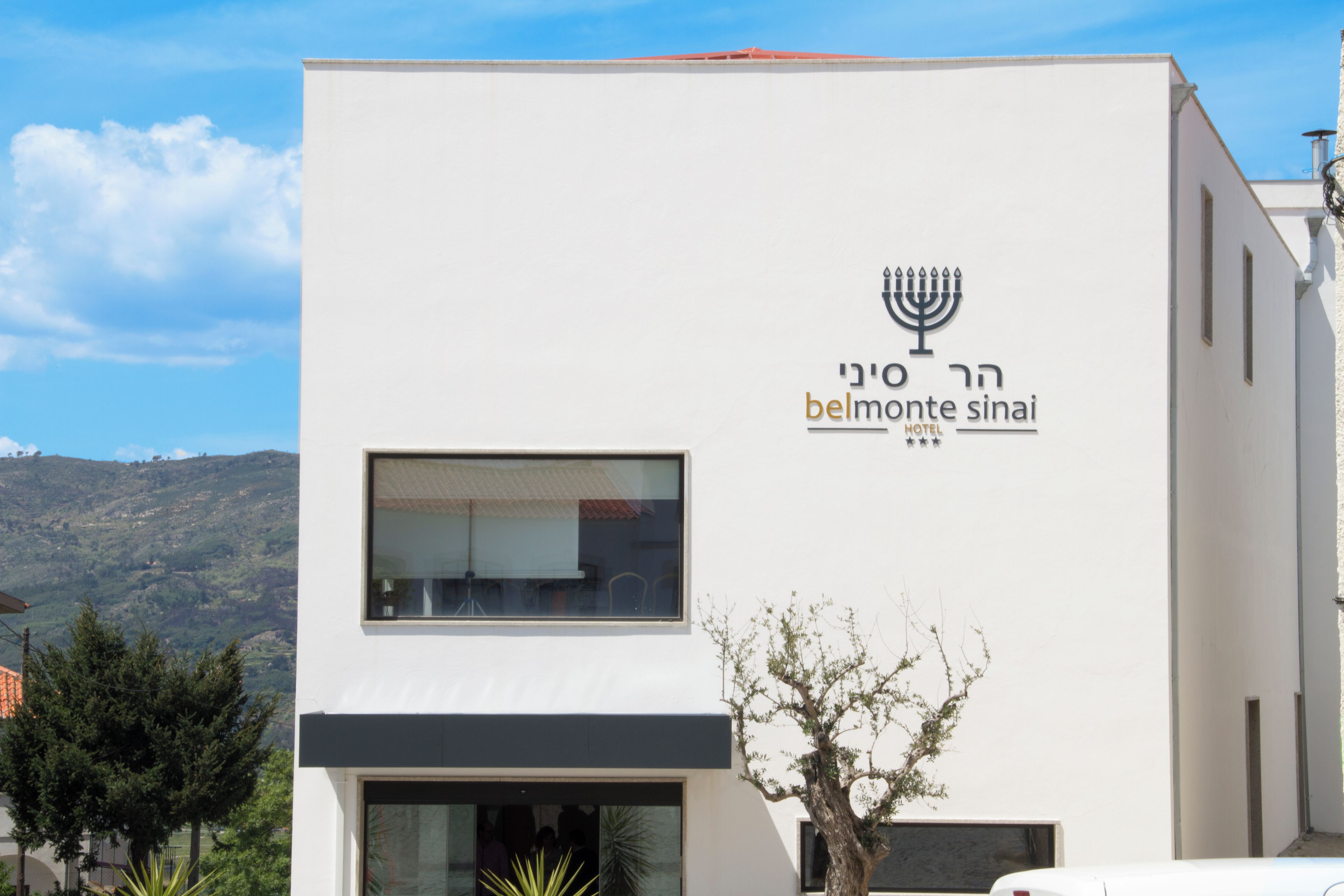 A modern building with a sign for 'Belmonte Sinai Hotel' featuring a menorah symbol.
