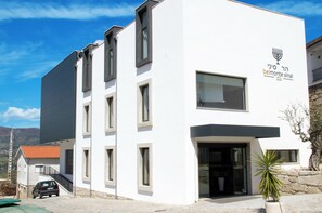 A modern building with a white facade, a visible entrance, and a logo with a menorah. - Belmonte Sinai Hotel (Belmonte)