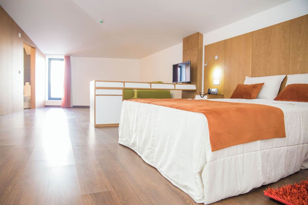 A modern hotel room with a bed, a desk, a television, and a view of the outside.